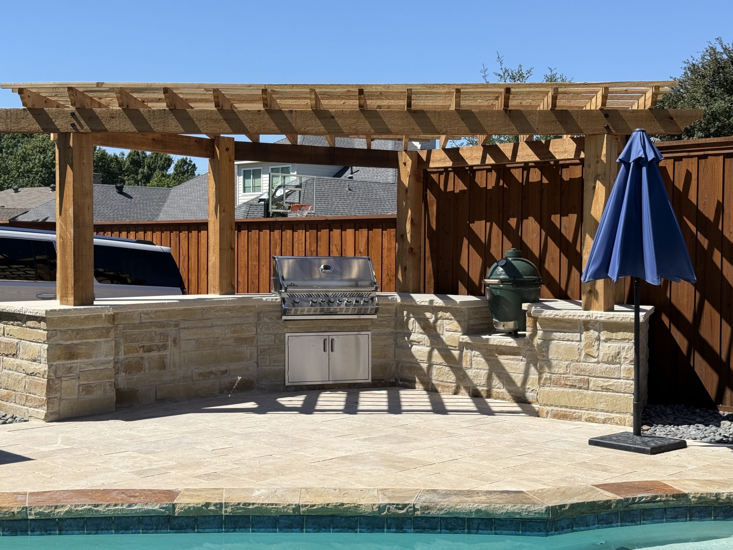 Outdoor grill under pergola by pool.