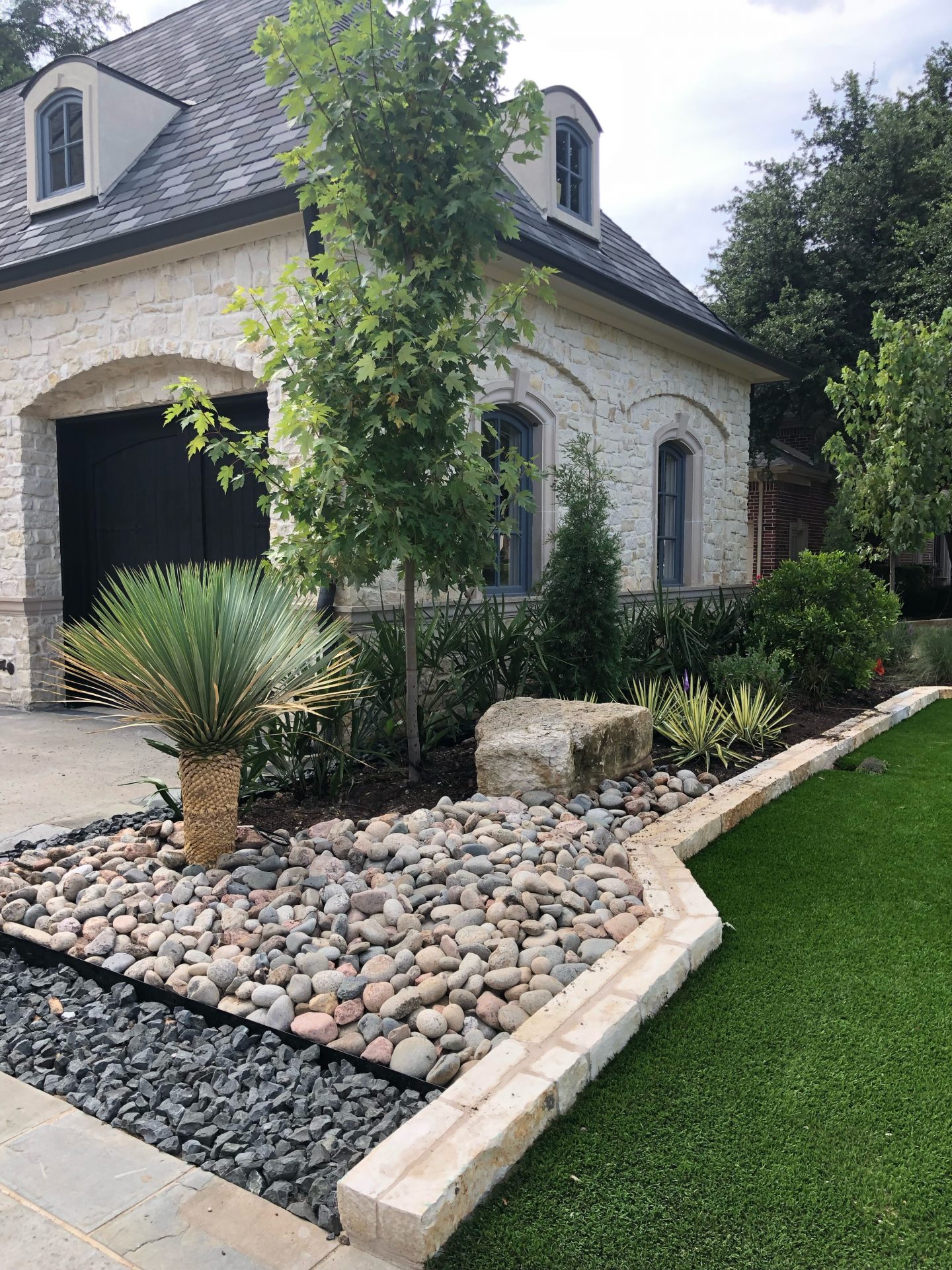 Stone house with landscaped garden and tree.