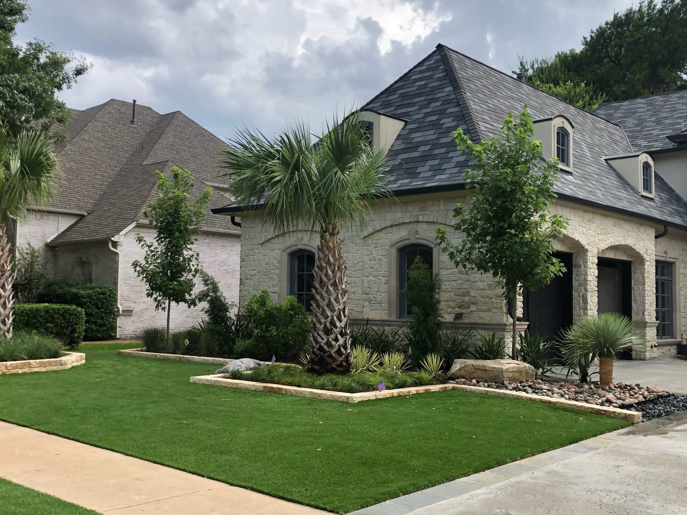 Stone house with manicured lawn and palm trees.
