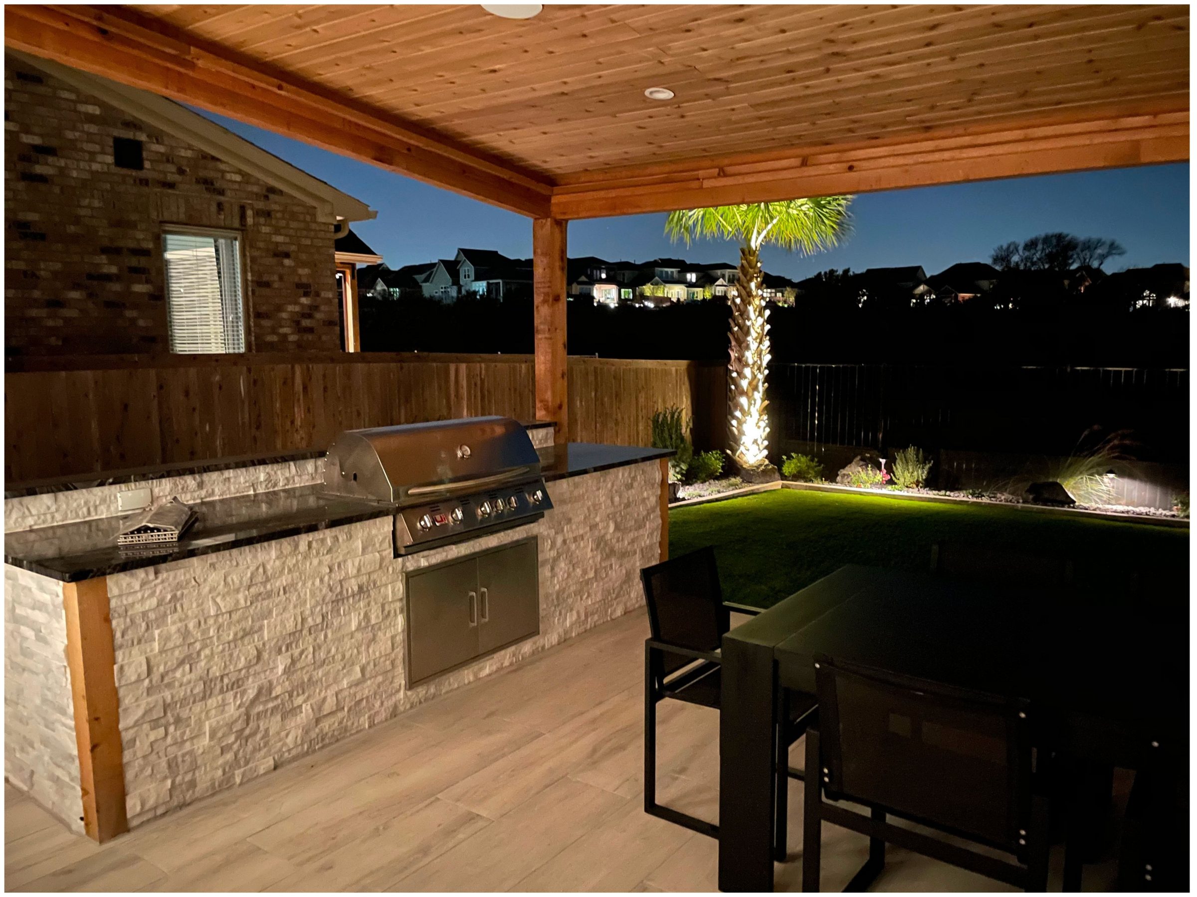 Covered outdoor kitchen patio with grill at night.