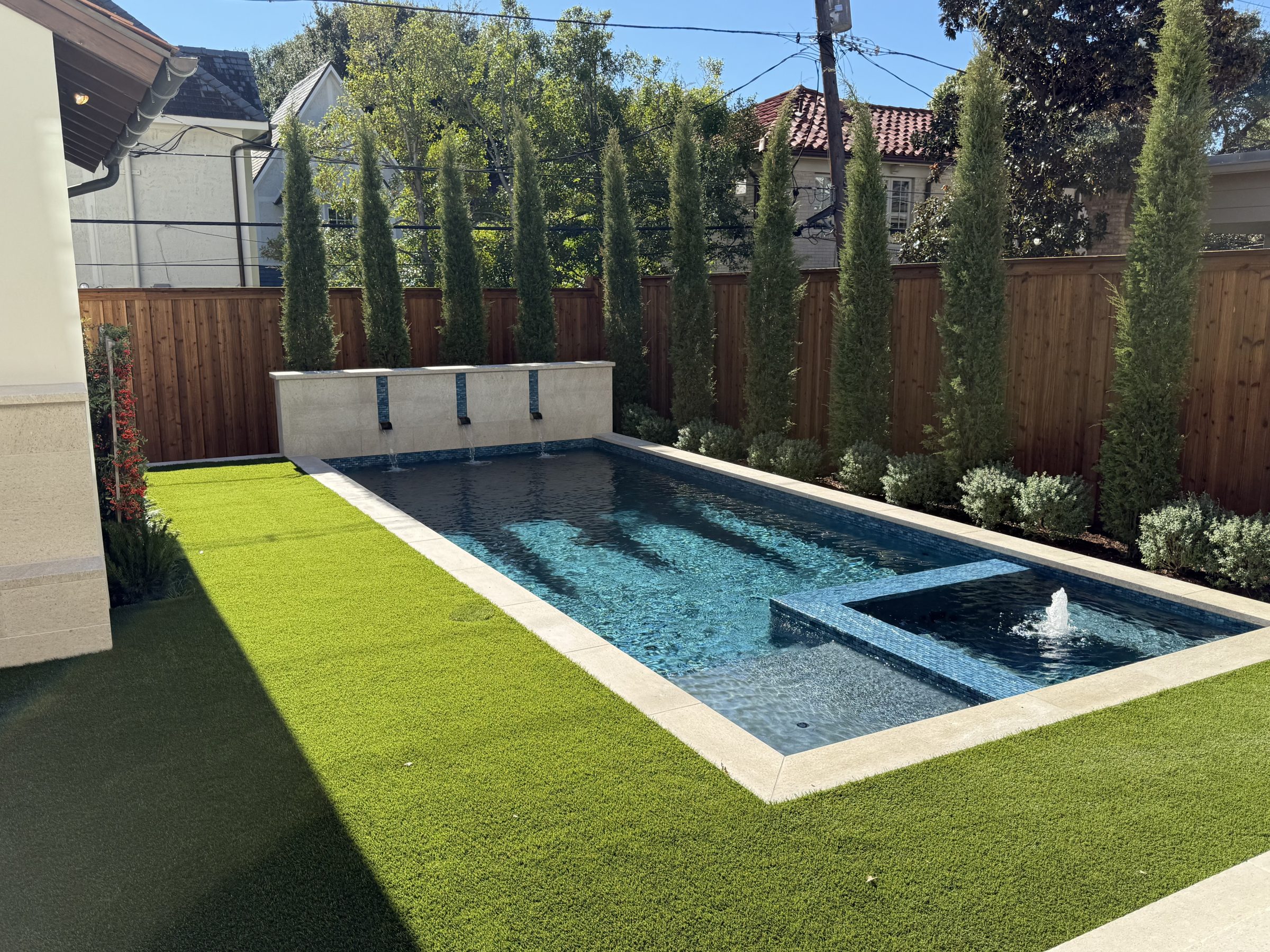 Modern backyard pool with fountain and greenery